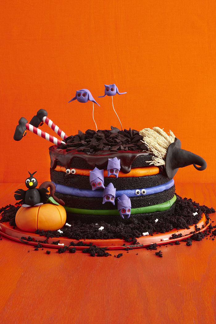 Witch halloween cake with colorful layers and purple bats on a bright orange background