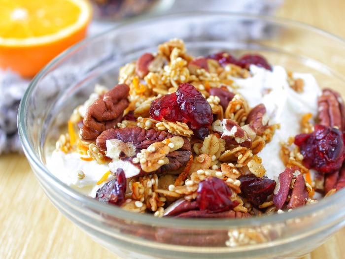 granola with pecans and cranberries in a glass bowl with milk and seeds