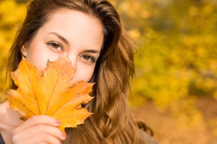 DIY Fall Wreathssmiling woman with a leave in front of her facr