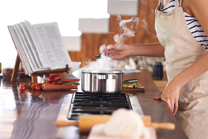 Woman with an apron cooking at home in the kitchen looking at a cookbook 