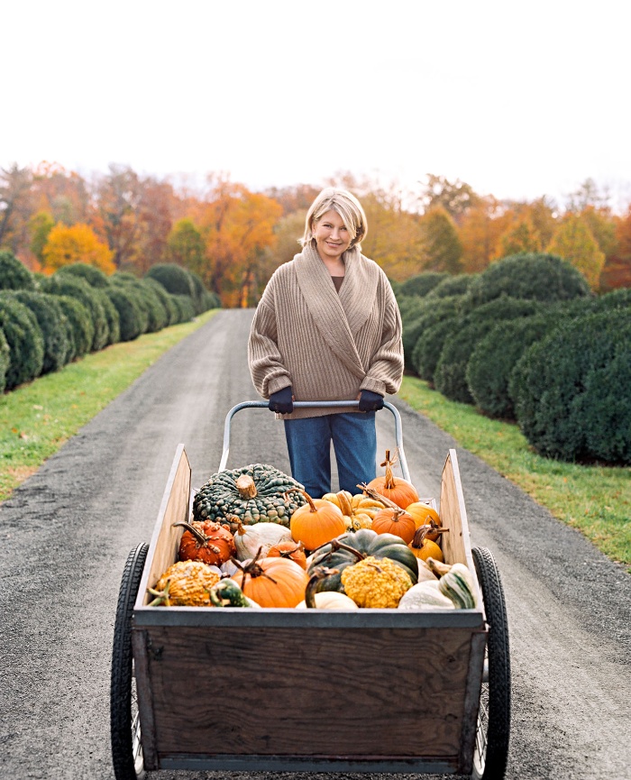 woman displaying fall harvest gourds and pumpkins in a beautiful yard