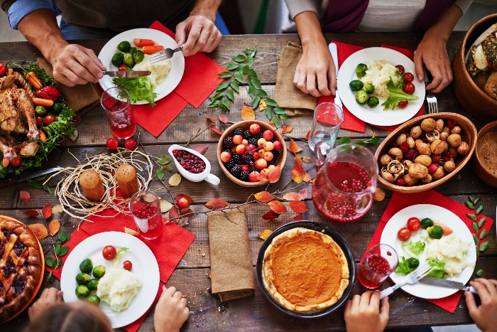 thanksgiving dinner table people sitting and easting colorful dishes on white plates and red napkins