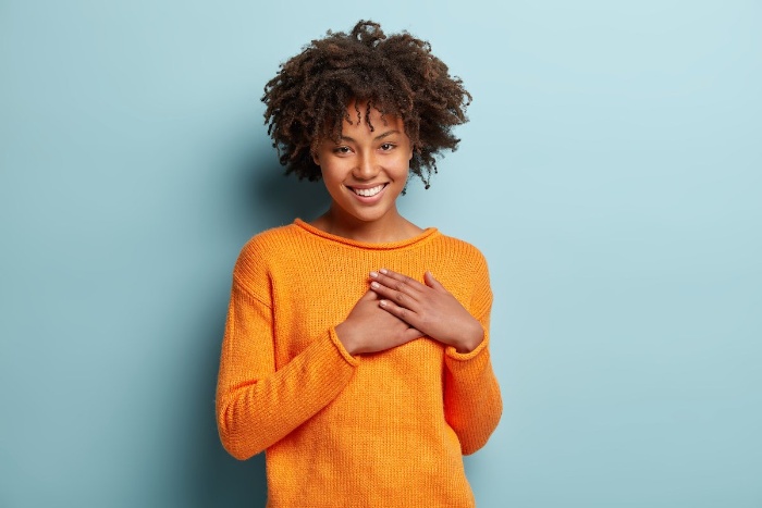 woman in yellow sweater smiling and holding her heart with two hands