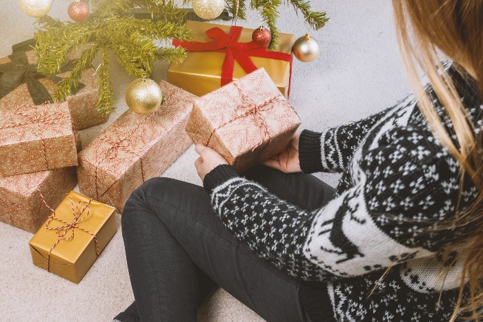 girls in jeans and winter sweater placing wrapped gifts under a christmas tree