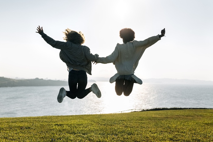 a couple holding hands and jumping in the air on a green field sea background