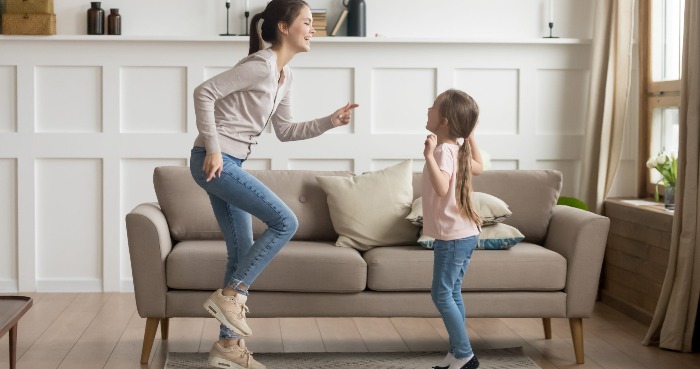 woman and little girl dancing and jumping indoors sofa and white wall in the background