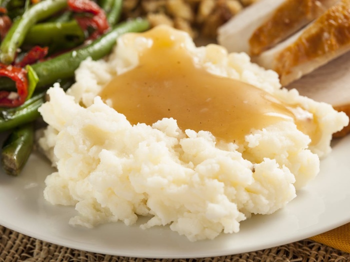 mashed potato dish with gravy in the middle on a plate with turkey and vegetables