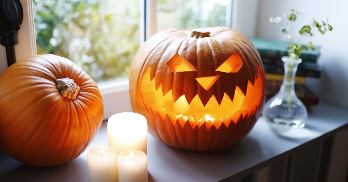 Thanksgiving decor carved pumpkin lanterns on a window sill with candles and a vase