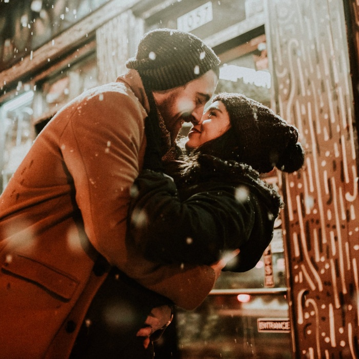 Couple outdoors dressed in winter clothes hugging and kissing in the snow