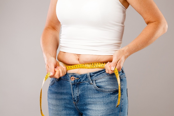 woman in jeans and white shirt measuring weigh gain with a meter 