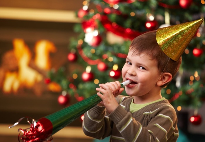 child with a golden party hat playing with a red and green paper trumpet 