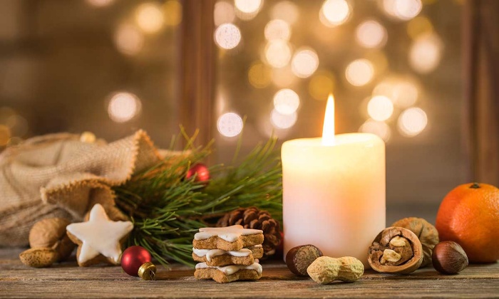 white christmas candle on a window sill surrounded by fruits nuts and glazed cookies