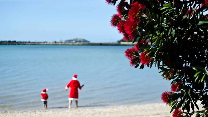 christmas in new zealand Santa and his helper on a beach in their costumes