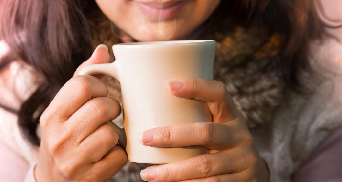 woman in a sweater holding a white mug with steaming hot beverage 