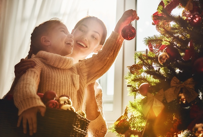 mother and daughter decorating the christmas tree in front of a window