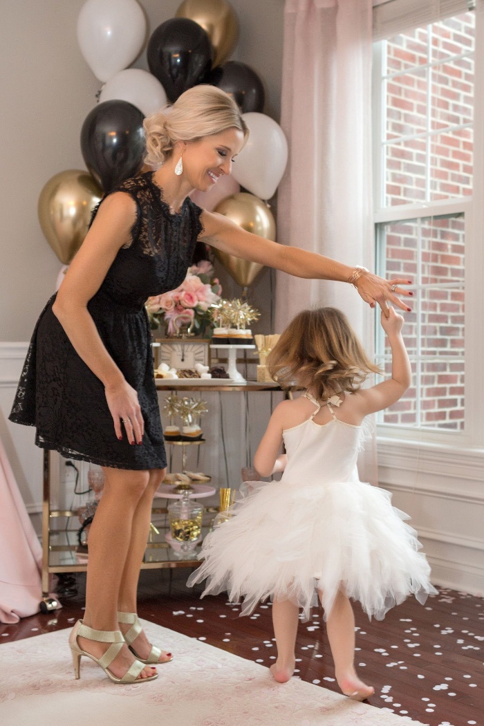 blond woman dressed in a black dress dancing with a little girl in a ballerina outfit