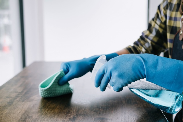 woman with blue gloves disinfecting a wooden table surface 