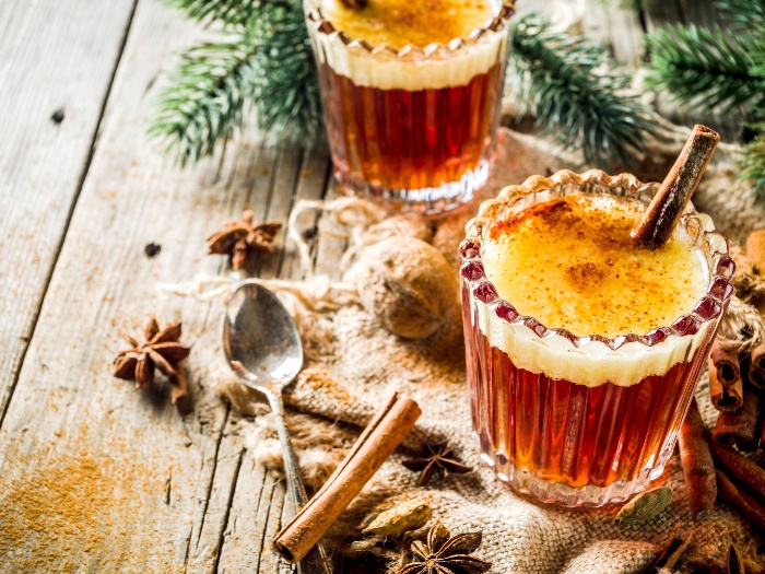 two warm drinks with cinnamon on a table decorated with winter spices