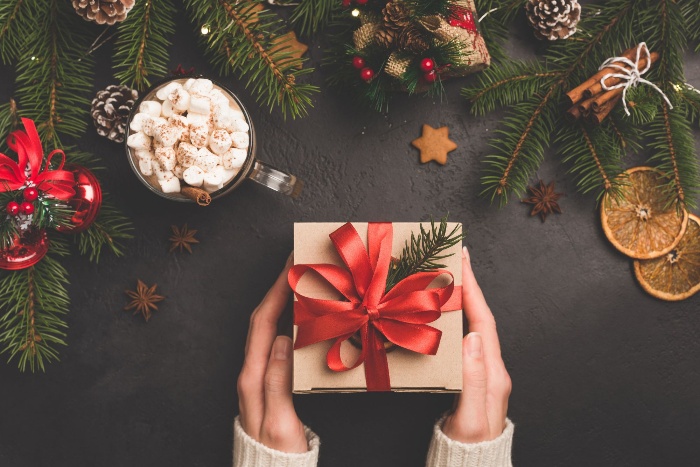 Christmas symbols two hands holding a box with red ribbon dried fruits cookies and pine branches