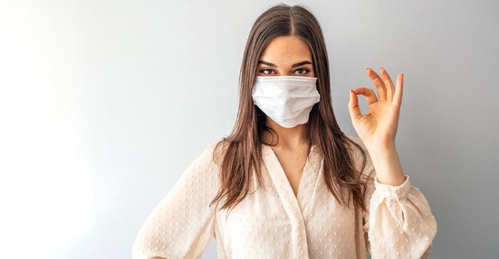 girl on a white background with a white face mask doing the ok sign with her fingers