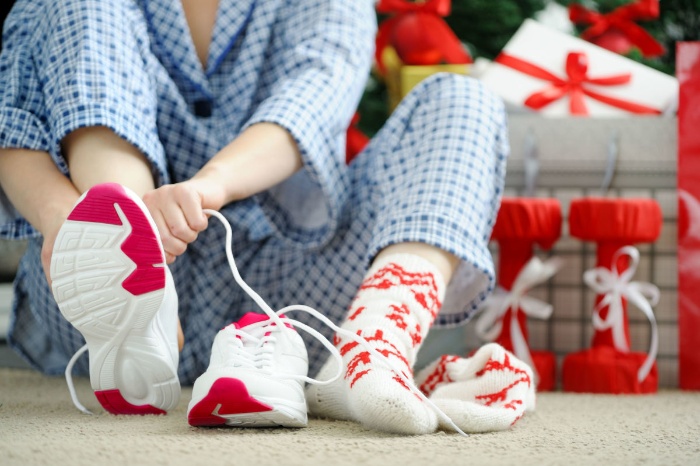 holiday fit woman in her pajamas putting her socks and sneakers on next to the christmas tree