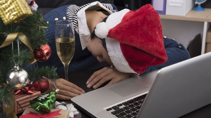 holiday hangover woman with a santa hat sleeping on her laptop with a champagne glass