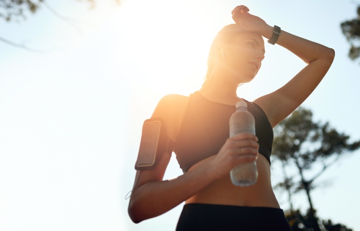 holiday workouts woman in sportwear with a bottle of water running outdoors phone on her arm