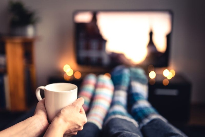 couple watching movies on a screen two pairs of feet in socks hands holding a mug