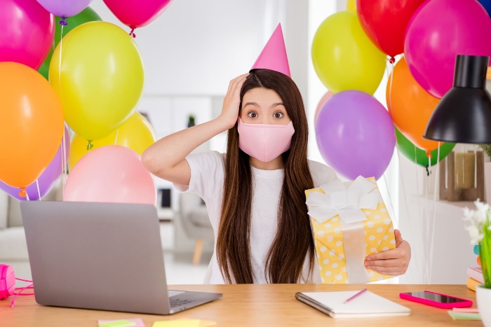 woman in front of her laptop with balloons and a present in her hand