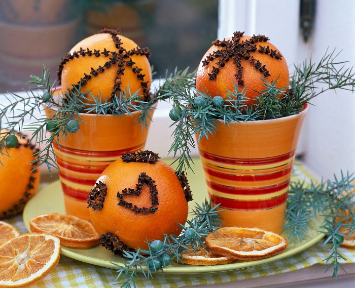 Oranges decorated with cloves on a plate with juniper