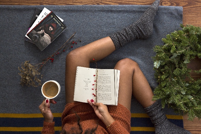 woman sitting on the floor reading a book with a coffee in her hand and holiday decor