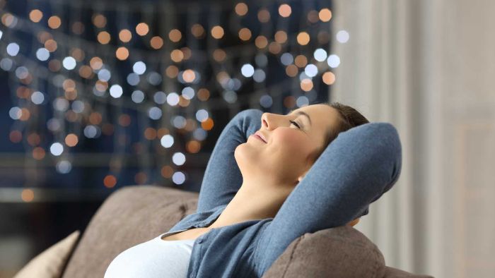 woman dressed in a blue cardigan lying on a sofa with her head and hands back