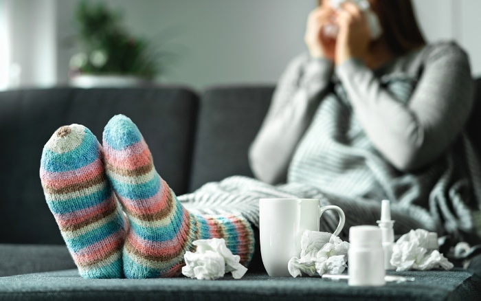 woman with socks sitting at home on the sofa sneezing flu season paper tissue