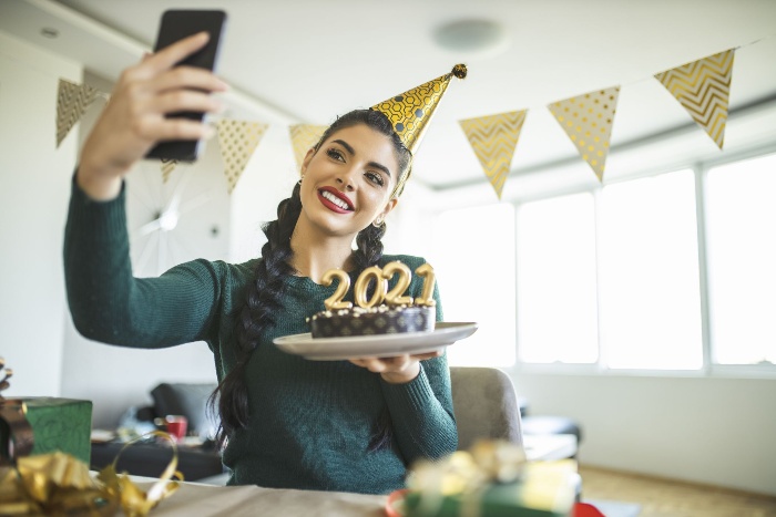 woman with a party hat holding a cake with 2021 sign and taking a selfie