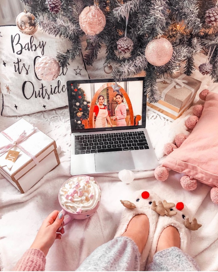 girl with a laptop under the christmas tree with deer slippers pink tree decor and pillows