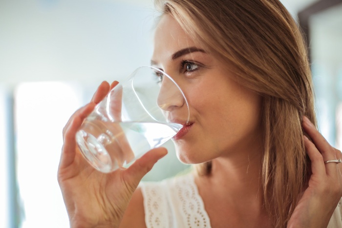 blond woman dressed in white drinking water from a glass cup