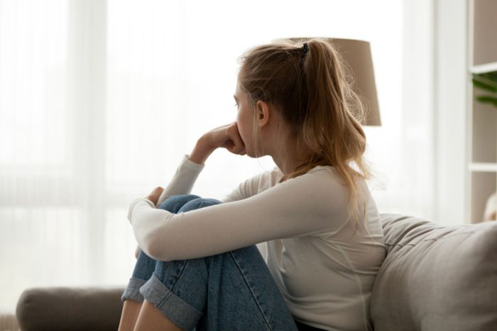 woman sitting on the sofa dressed in jeans with her legs up looking through the window