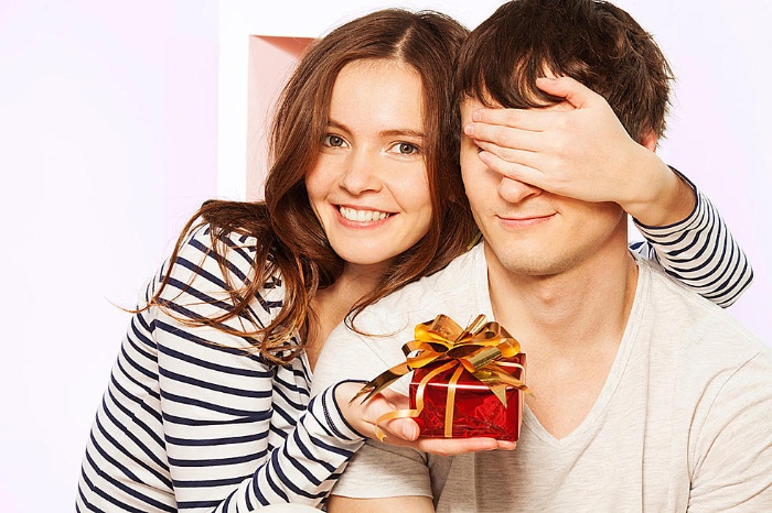 woman in striped shirt giving a man a little gift covering his eyes with her hand