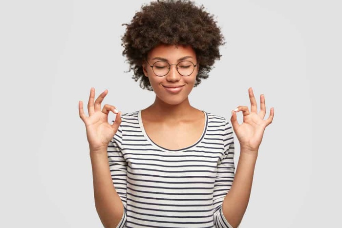 woman with an afro hairstyle and striped shirt and glasses meditating 