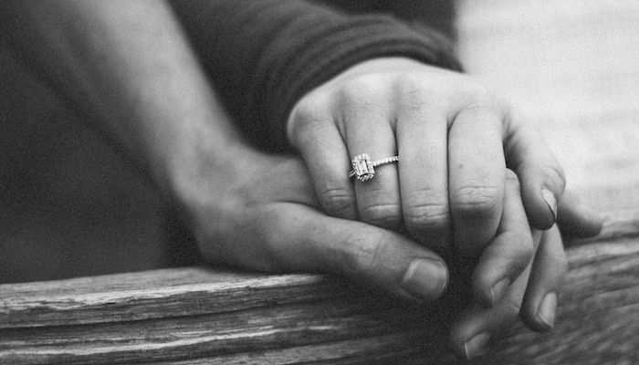 black and white picture two people holding hands woman with an engagement ring 