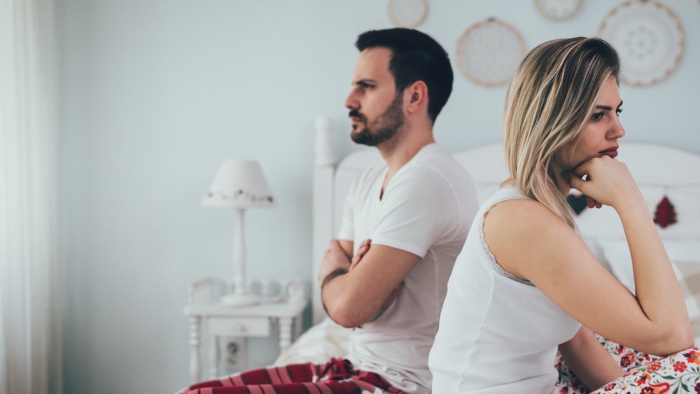 couple in conflict man and woman in white tops standing on a bad with their backs to each other