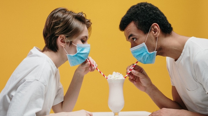 couple with masks on a yellow background drinking shake from two straws 