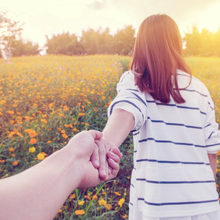 couple holding hands walking outside in a field of flowers