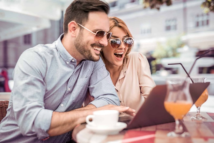 a man and a woman looking at a laptop with their sun glasses on drinking orange juice