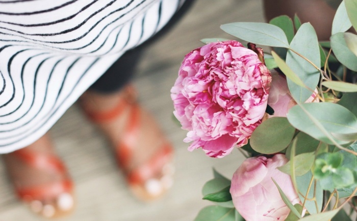 close up pink peony flower in the background woman with sandals and striped shirt