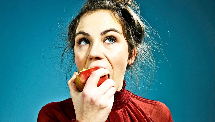 woman in a red shirt eating an apple on a blue background
