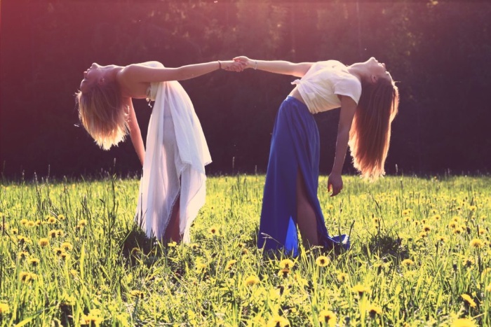 feminine energy two women in dresses on a green field holding hands and bending backwards