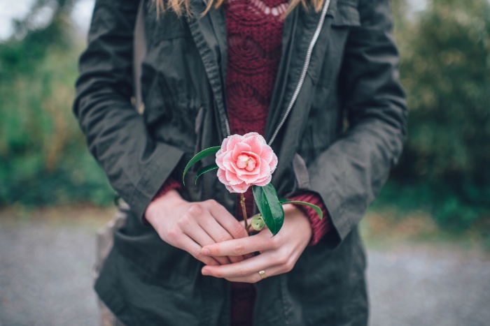 woman dressed in a black jacket holding a pink flower in her hands