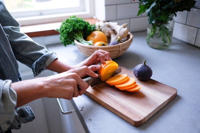 woman in a shirt cutting fruits on a cutting board in a kitchen