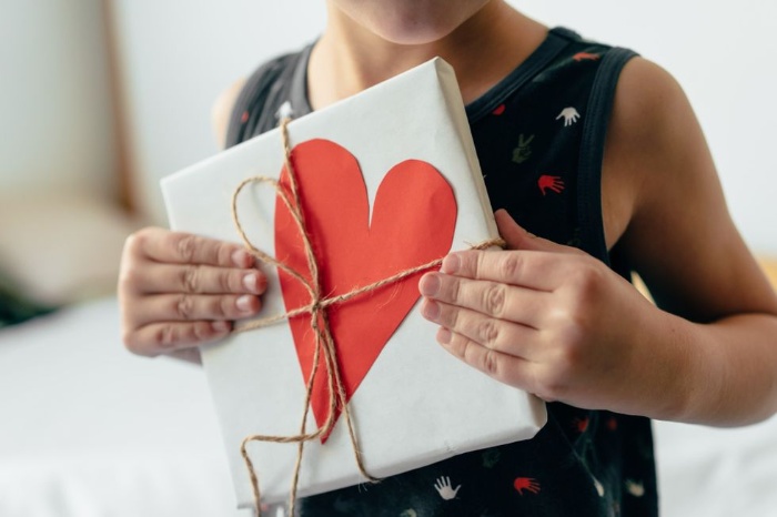 child holding a fun gift wrapped in white paper with a red heart